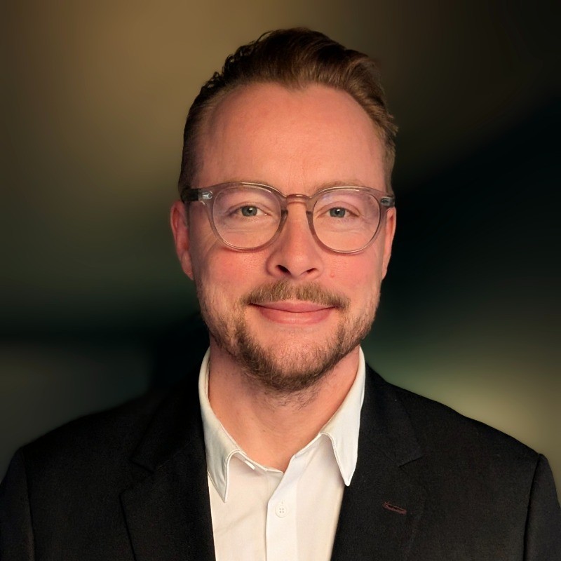 Frederik Nicolaisen, Sikkerhetssjef i Eika, smiler mot kamera i portrett med mørk bakgrunn.