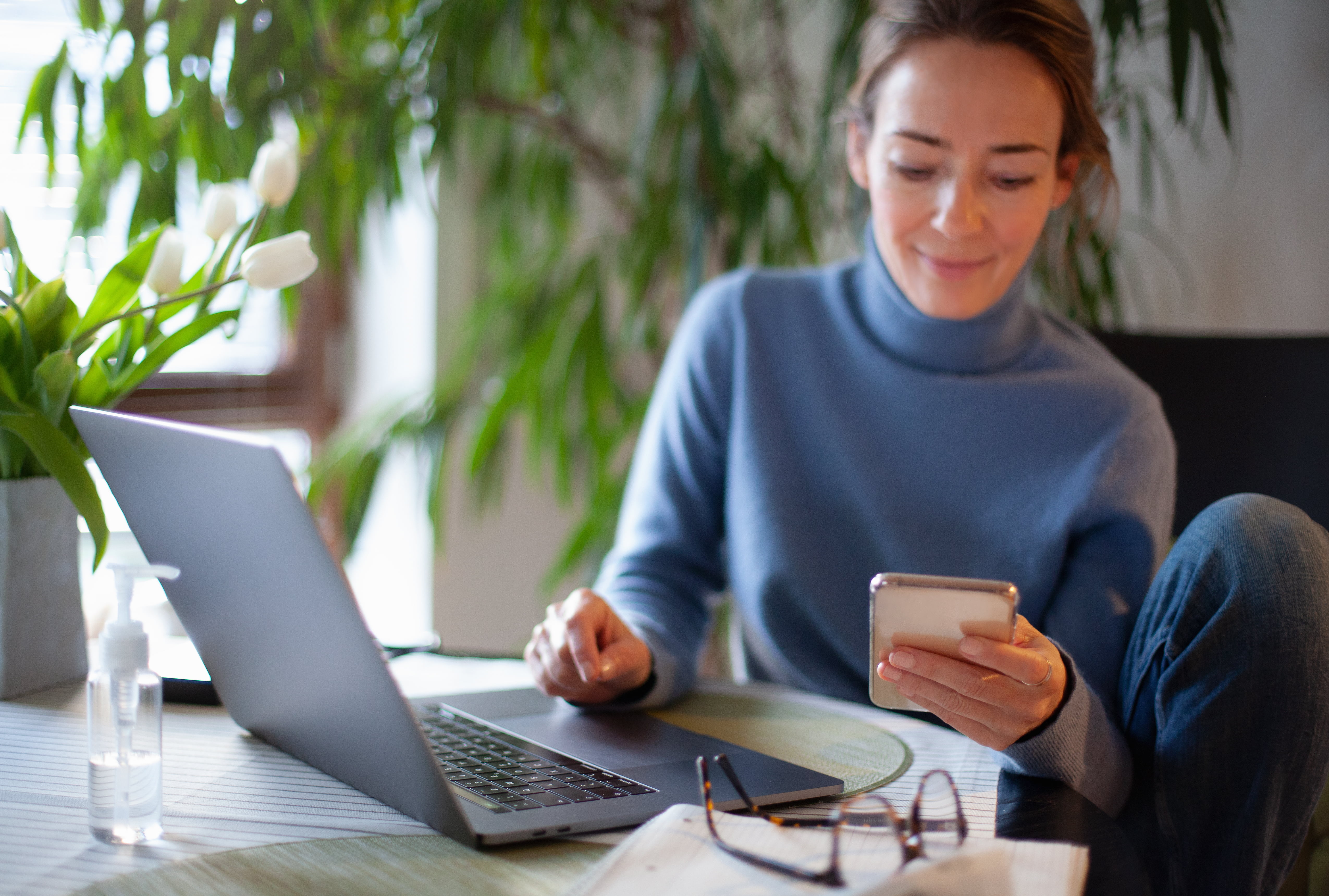 Ung kvinne med telefon og laptop paa kontor