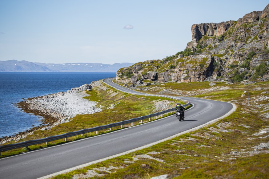 Motorsyklist kjører langs vei ved havet