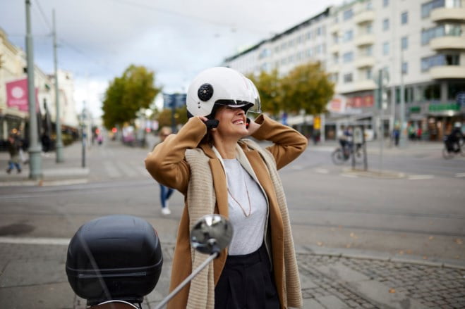 Dame som tar på seg en hjelm før hun setter seg på mopeden sin